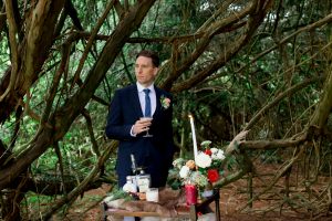 groom with a drink under a tree at a garden wedding