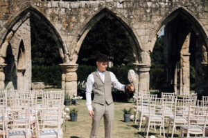 A man stands with an owl on his arm among empty wedding chairs