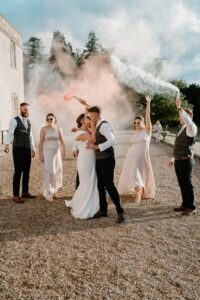 bridesmaids and groomsmen holding smoke sticks over bride and groom